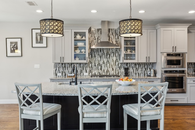 kitchen with wall chimney range hood, tasteful backsplash, a kitchen bar, and visible vents