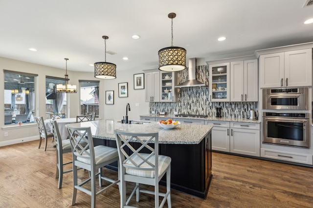 kitchen with wall chimney range hood, a breakfast bar area, backsplash, a sink, and light stone counters