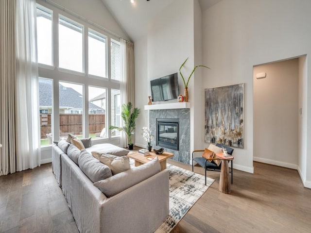 living room featuring baseboards, high vaulted ceiling, a tiled fireplace, and wood finished floors