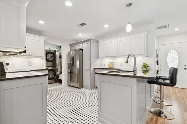 kitchen with visible vents, stacked washer and clothes dryer, dark countertops, stainless steel fridge, and a sink