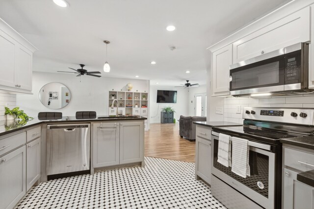 kitchen featuring a ceiling fan, dark countertops, appliances with stainless steel finishes, a sink, and a peninsula