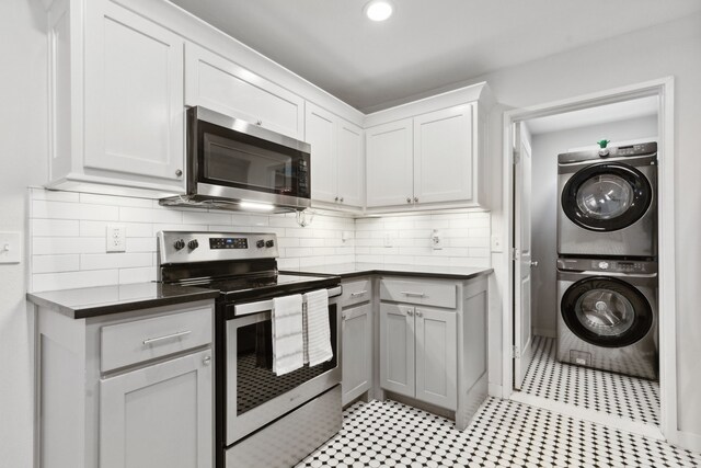 kitchen with decorative backsplash, stainless steel appliances, stacked washer / drying machine, and dark countertops