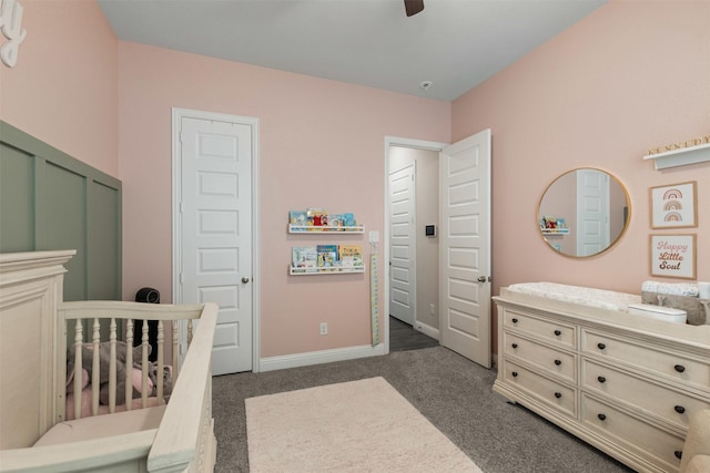 bedroom with dark carpet, a ceiling fan, a crib, and baseboards