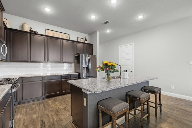kitchen featuring decorative backsplash, dark brown cabinetry, dark wood-style flooring, a sink, and stainless steel appliances