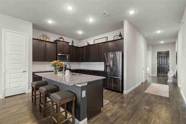kitchen featuring a breakfast bar area, tasteful backsplash, dark brown cabinets, a sink, and stainless steel appliances