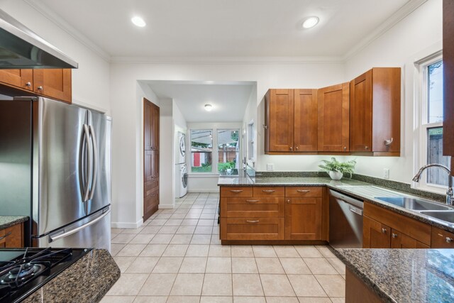 906 N Clinton Ave, Dallas, TX 75208 - kitchen featuring stacked washer / dryer, wall chimney exhaust hood, brown cabinets, a sink, and stainless steel appliances
