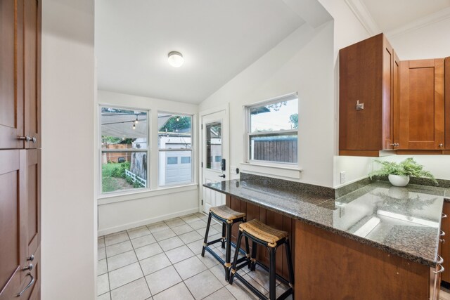 906 N Clinton Ave, Dallas, TX 75208 - kitchen with brown cabinetry, light tile patterned flooring, a breakfast bar area, dark stone counters, and vaulted ceiling