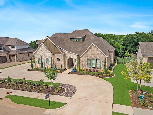 french country inspired facade with board and batten siding, brick siding, curved driveway, and a front lawn