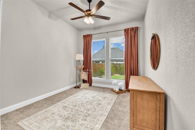 interior space with a ceiling fan, baseboards, light colored carpet, and a textured wall