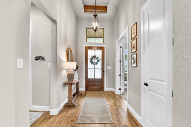 entryway with light wood-style floors, baseboards, and a raised ceiling