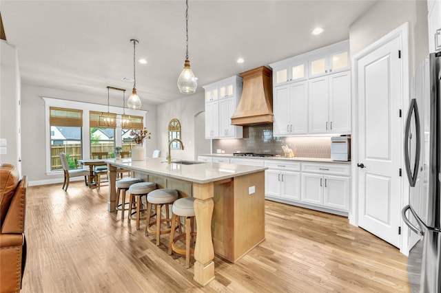 kitchen with stainless steel appliances, a sink, light wood finished floors, and custom range hood