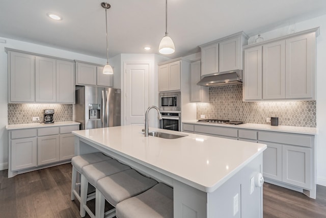 kitchen featuring backsplash, appliances with stainless steel finishes, a sink, under cabinet range hood, and dark wood-type flooring