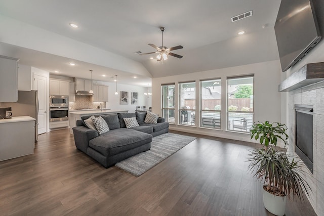 living area with ceiling fan, a fireplace, lofted ceiling, dark wood-type flooring, and visible vents