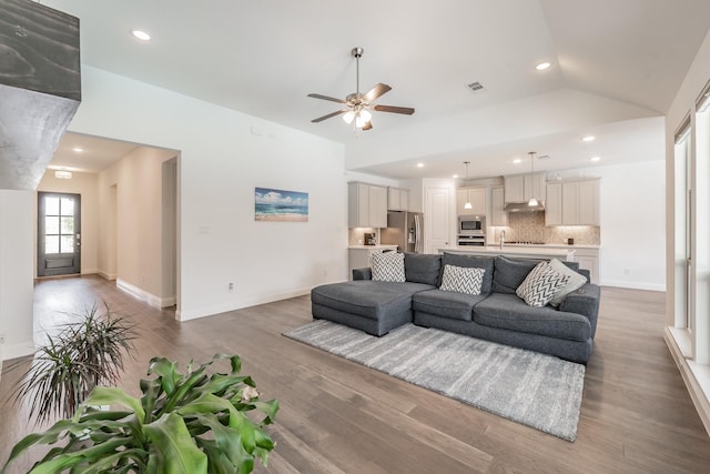 living area with ceiling fan, visible vents, baseboards, wood finished floors, and vaulted ceiling