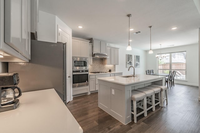 kitchen featuring backsplash, a sink, light countertops, under cabinet range hood, and stainless steel appliances