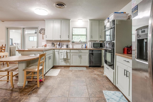 kitchen featuring a peninsula, a breakfast bar, light countertops, a textured ceiling, and appliances with stainless steel finishes