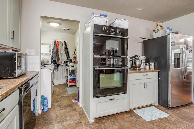 kitchen with white cabinets, a textured ceiling, stone finish floor, washer / clothes dryer, and stainless steel appliances