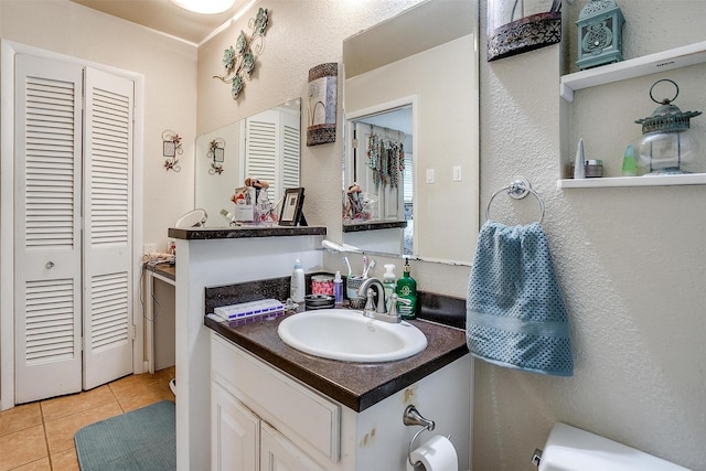half bathroom featuring tile patterned flooring, a textured wall, toilet, and vanity