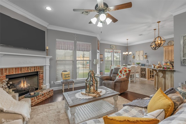 living room with visible vents, ornamental molding, ceiling fan with notable chandelier, and a fireplace