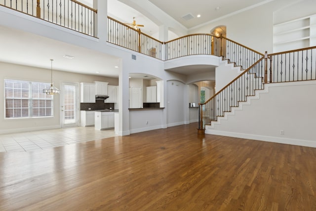 unfurnished living room with a notable chandelier, light wood finished floors, arched walkways, stairs, and baseboards