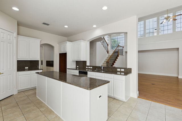 kitchen with arched walkways, white cabinetry, decorative backsplash, light tile patterned floors, and visible vents