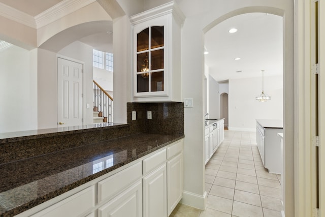 kitchen featuring white cabinets, arched walkways, dark stone countertops, light tile patterned floors, and glass insert cabinets