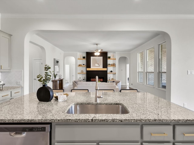 kitchen featuring ceiling fan, a sink, arched walkways, gray cabinets, and stainless steel dishwasher