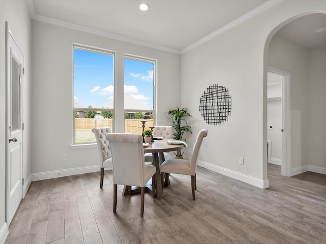 dining space with crown molding, arched walkways, baseboards, and wood finished floors
