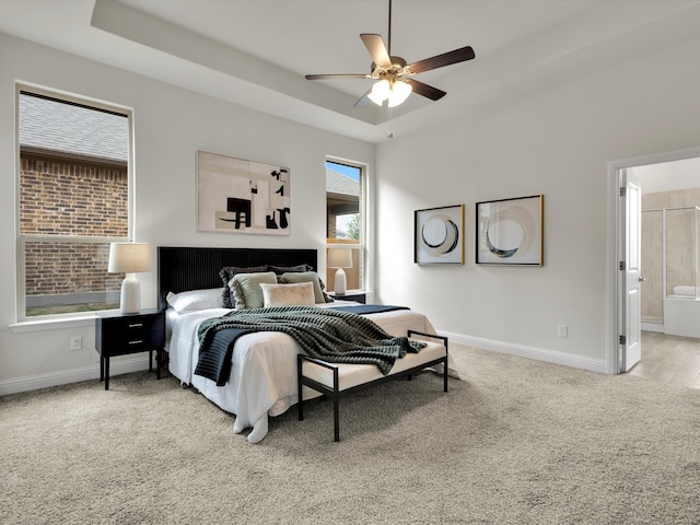 carpeted bedroom featuring baseboards, a ceiling fan, a tray ceiling, and ensuite bath