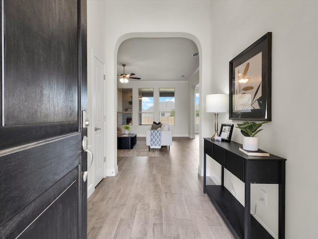 foyer entrance with light wood-style floors, arched walkways, baseboards, and a ceiling fan