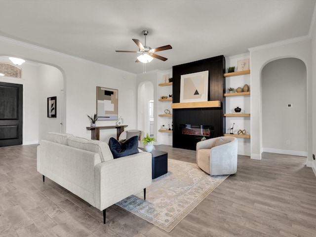 living area featuring ornamental molding, baseboards, light wood-style floors, ceiling fan, and arched walkways