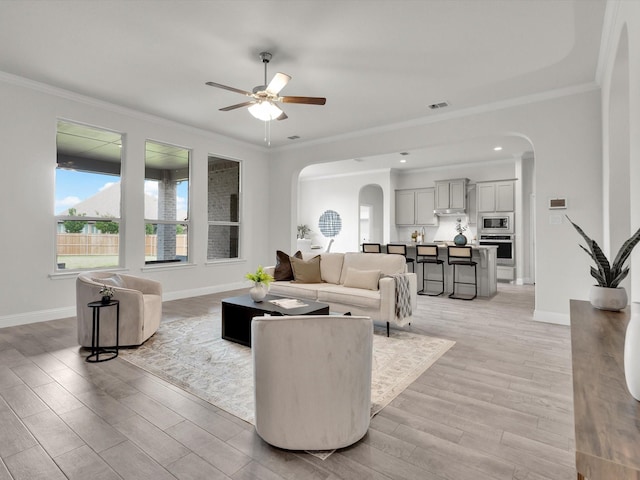 living area featuring arched walkways, ornamental molding, baseboards, and ceiling fan