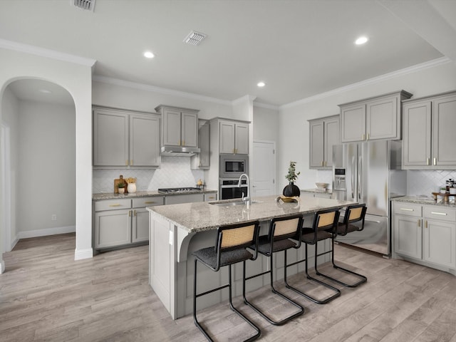 kitchen featuring appliances with stainless steel finishes, a sink, visible vents, arched walkways, and gray cabinetry