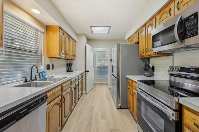 kitchen featuring a sink, light wood-style floors, light countertops, stainless steel appliances, and decorative backsplash