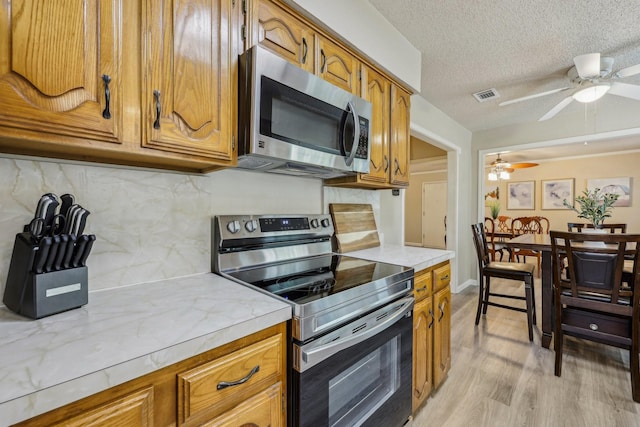 kitchen featuring appliances with stainless steel finishes, light countertops, brown cabinetry, a ceiling fan, and visible vents