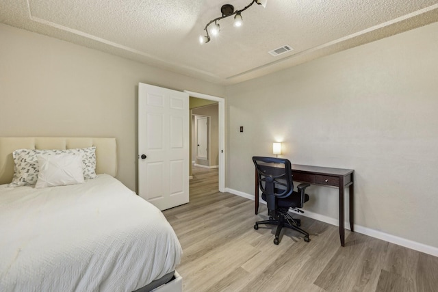 bedroom featuring a textured ceiling, baseboards, wood finished floors, and visible vents