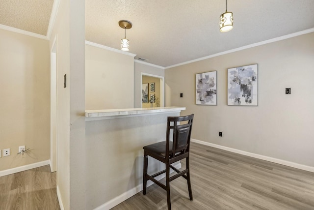 bar featuring crown molding, visible vents, wood finished floors, baseboards, and decorative light fixtures