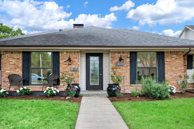 view of front facade featuring roof with shingles, a front lawn, and brick siding
