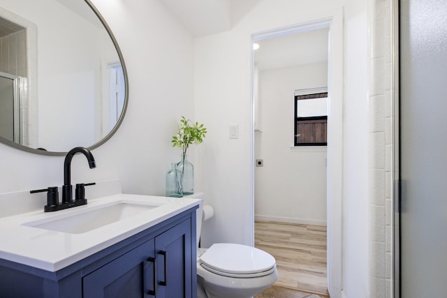bathroom featuring wood finished floors, vanity, baseboards, toilet, and a shower with door