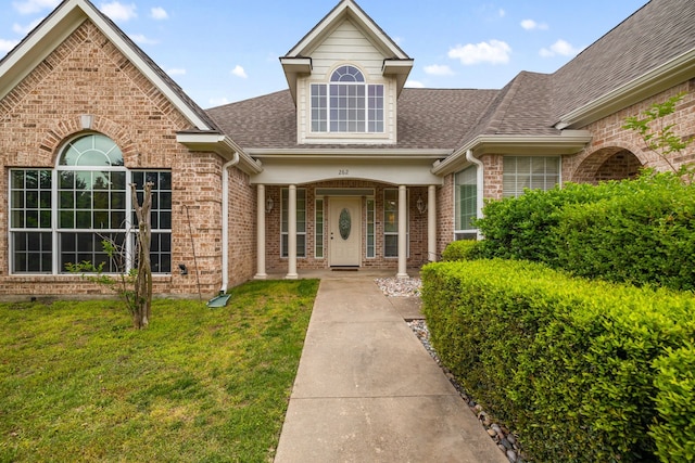 doorway to property featuring brick siding, a shingled roof, and a yard