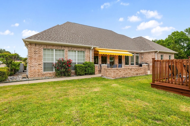 rear view of property featuring brick siding, a shingled roof, a lawn, and fence