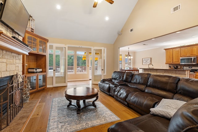 living room with high vaulted ceiling, a stone fireplace, ceiling fan with notable chandelier, recessed lighting, and visible vents