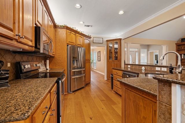 kitchen with a sink, brown cabinetry, light wood-style flooring, stainless steel appliances, and backsplash