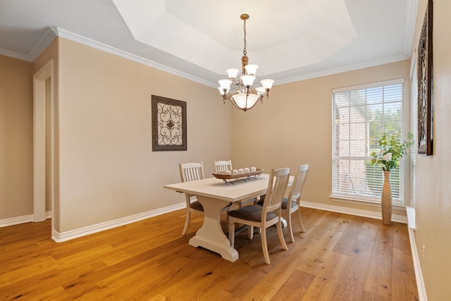 dining area featuring light wood finished floors, a chandelier, baseboards, a tray ceiling, and ornamental molding