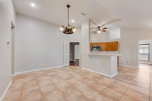 kitchen with brown cabinetry, visible vents, stainless steel microwave, ceiling fan with notable chandelier, and light tile patterned flooring