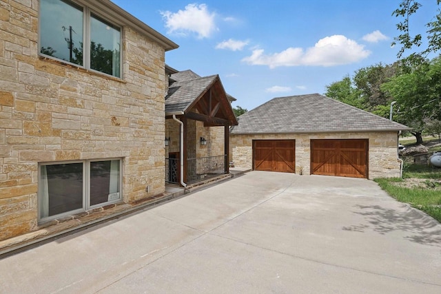 exterior space with a shingled roof, stone siding, and a garage