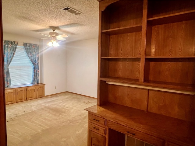 interior space featuring a ceiling fan, a textured ceiling, visible vents, baseboards, and light carpet
