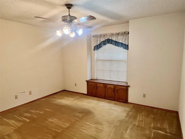 unfurnished dining area featuring a ceiling fan, a textured ceiling, light colored carpet, and baseboards