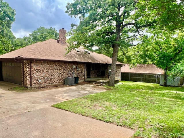 back of house with a garage, fence, a chimney, brick siding, and a yard