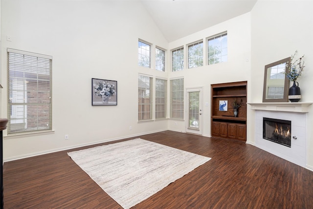 unfurnished living room with dark wood-style flooring, high vaulted ceiling, baseboards, and a tile fireplace